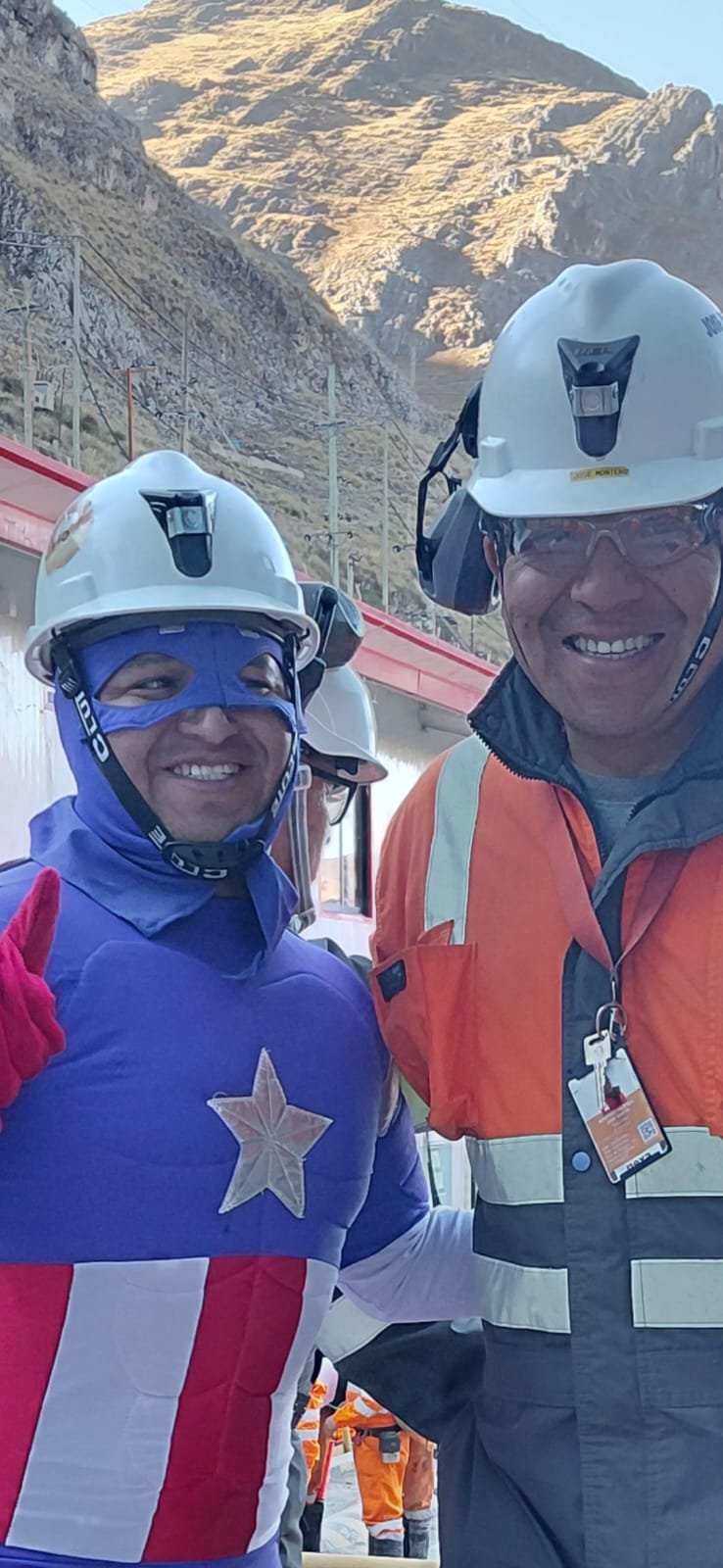 Dos personas con casco sonriendo durante una campaña de seguridad; una lleva un disfraz de superhéroe