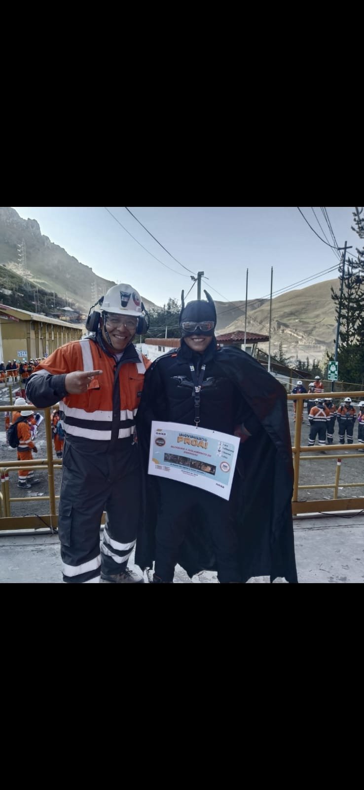 Trabajador con casco y protectores auditivos junto a una persona disfrazada de superhéroe que sostiene un cartel sobre bloqueo y aislamiento de energías