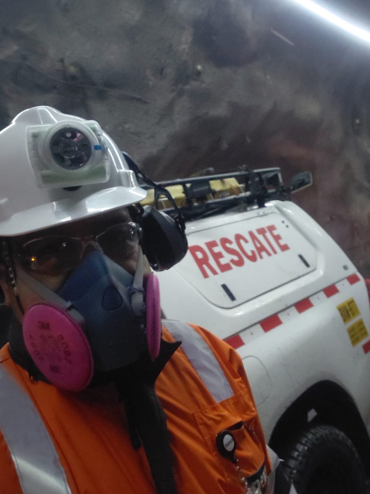 Persona con casco con lámpara, lentes y respirador junto a una camioneta de rescate dentro de una mina subterránea